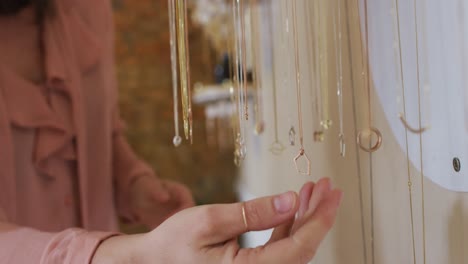 close up of hand of caucasian woman touching golden necklaces hanging on rack, shopping for jewelry