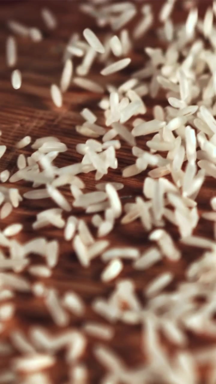 Movimento rallentato di chicchi di riso crudo che cadono su una superficie in legno