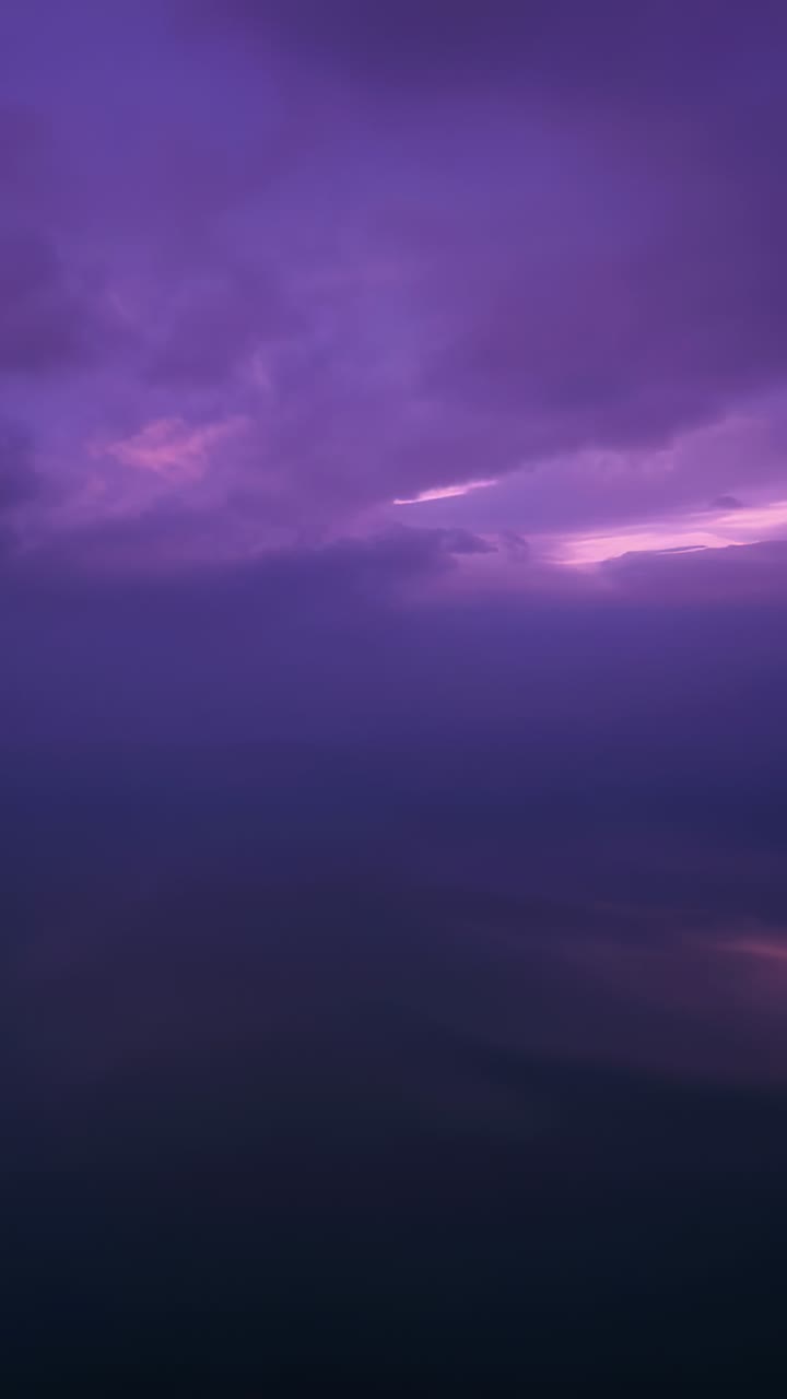 Video verticale: Nuvole viola stratificate si muovono reagendo a un bagliore a destra sopra l'acqua scura, riflettendo.