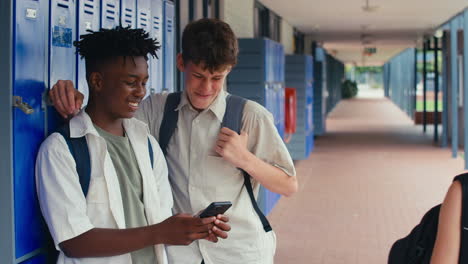 two male high school or secondary students looking at social media or internet on phone by lockers