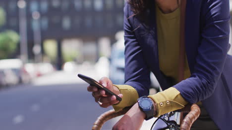 african american woman using smartphone in street leaning on bicycle