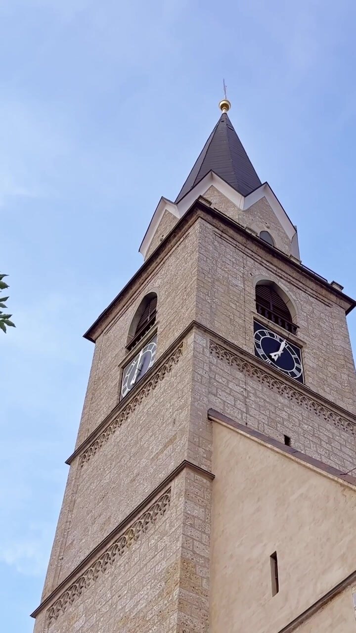 Torre do relógio de pedra da Igreja de São Cantiano contra o céu azul em Kranj, Eslovênia, com revelação vertical além do primeiro plano