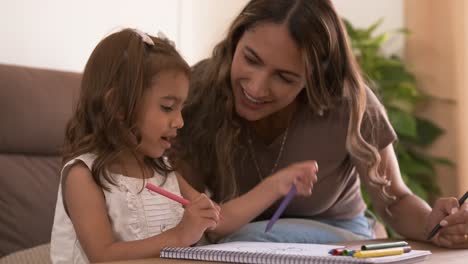 happy mother and daughter drawing in book together at home