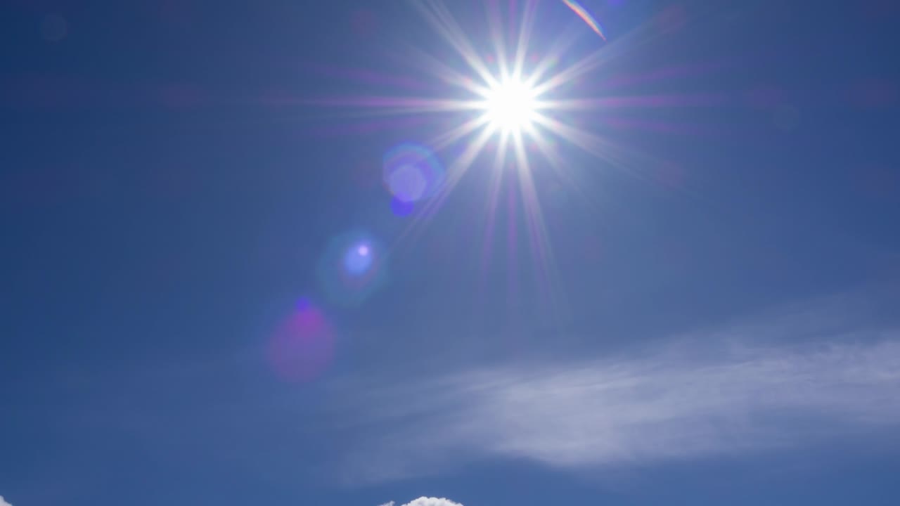 Sunstar's beautiful beams and lens flare in clear blue sky on a bright sunny day in the mid-spring season. wispy clouds moving past through sunlight in mid-day. hight in sky. sun heat creates energy