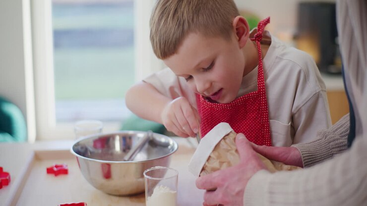 Boy Works In The Kitchen And Pours Flour Into The Dough And Kneads It
