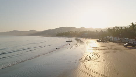 Rising-sunrise-aerial-of-fishing-boat-sitting-in-waves-on-tropical-beach,-4K