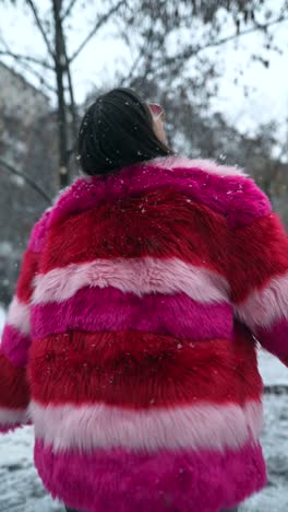 mujer con un abrigo de piel rosa y rojo disfrutando de la nieve