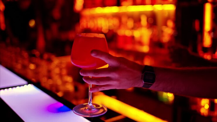 Un barman che prepara un cocktail con un alcolico amaro al bar di notte con luci al neon rosse, slow motion