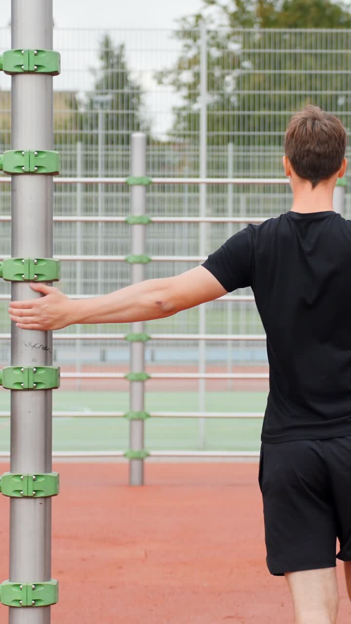 Man warms up outdoors with stretches on sports field, focused and calm, vertical