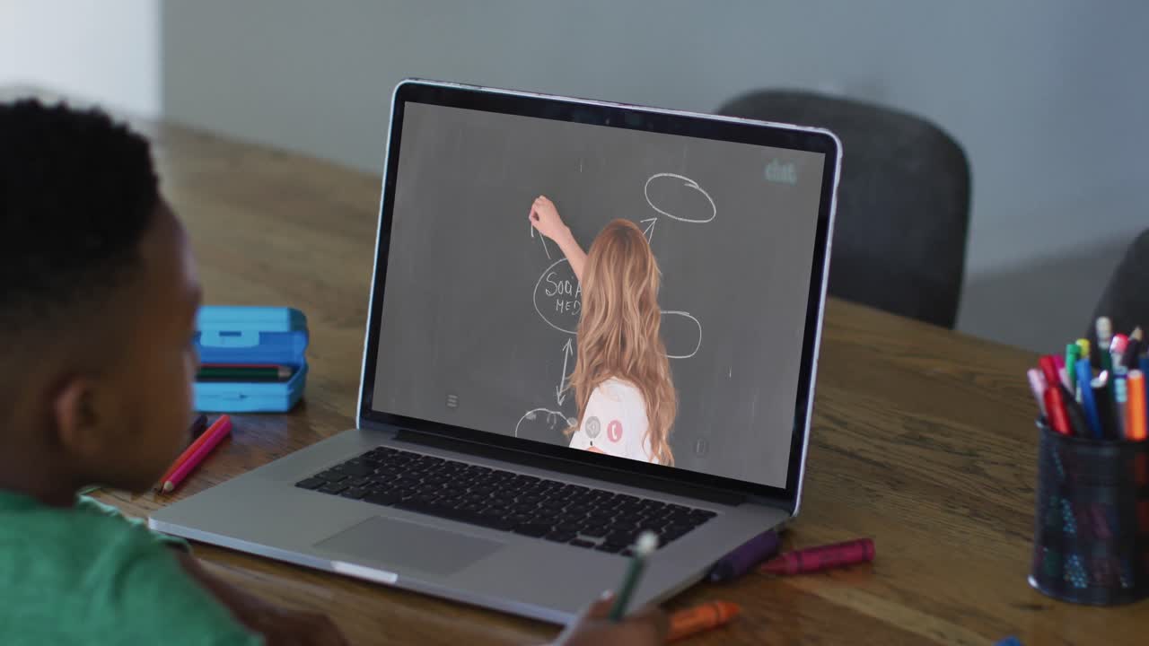 niño afroamericano haciendo una videollamada en una computadora portátil mientras hace la tarea en casa