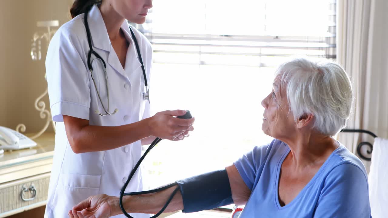 Female doctor checking the blood pressure of senior woman in the bedroom