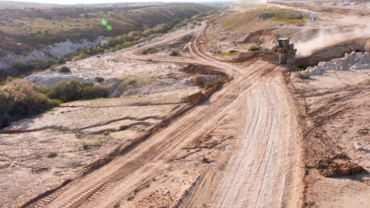 Aerial of front end loader digging machine driving on dusty dirt road at work site