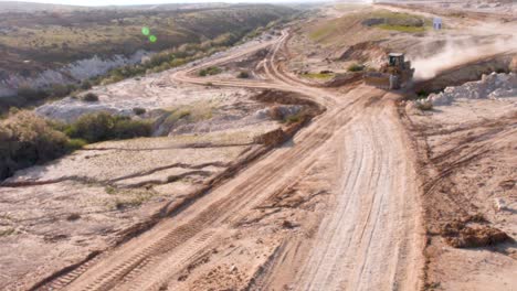 aerial of front end loader digging machine driving on dusty dirt road at work site