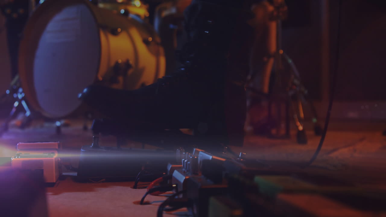 Pedali per effetti per chitarra che brillano sul pavimento del palco tra cavi e hardware della batteria sfocato in un rendering 3D.