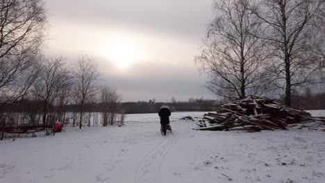 mother push baby carriage on snowy countryside yard near wood pile