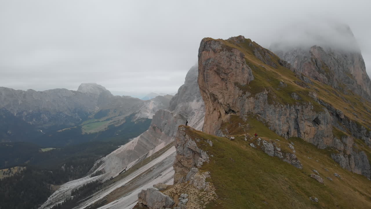toma circular aérea de un dron de un joven modelo masculino parado al borde de una roca en seceda, italia