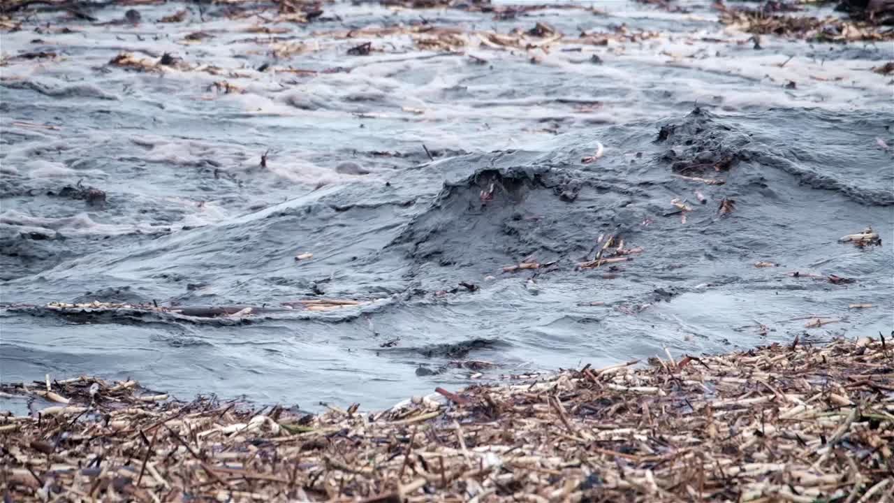 Acqua fangosa e nera piena di detriti scorre turbolentemente