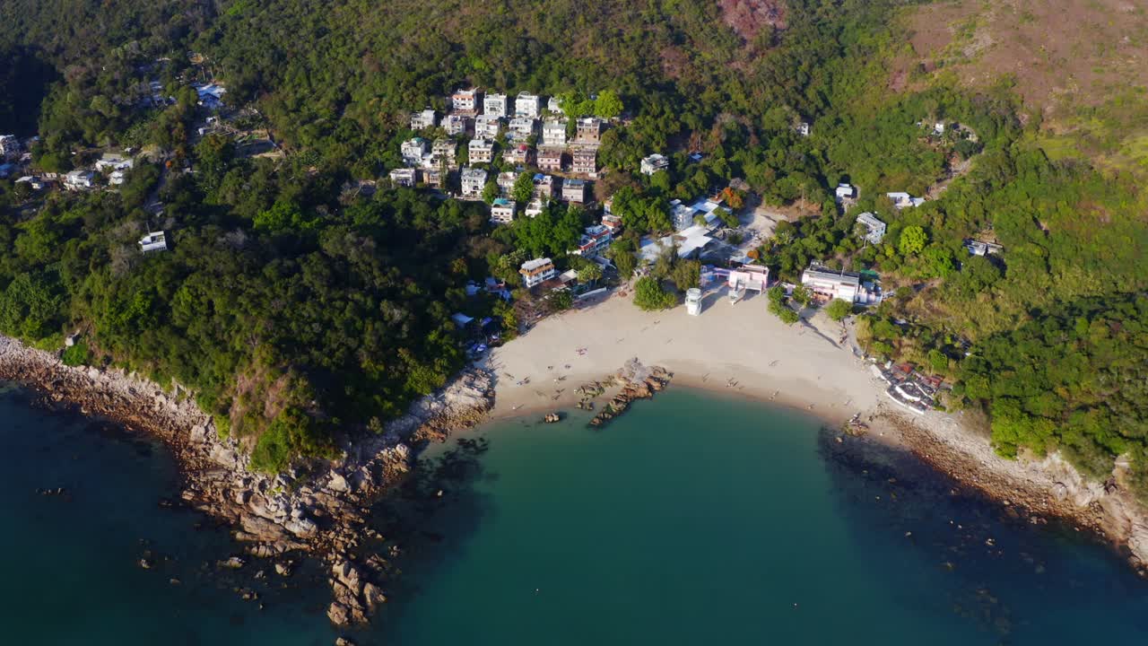 disparo de drones viajando hacia adelante sobre pequeños pueblos con una playa entre las montañas y el bosque durante un día soleado
