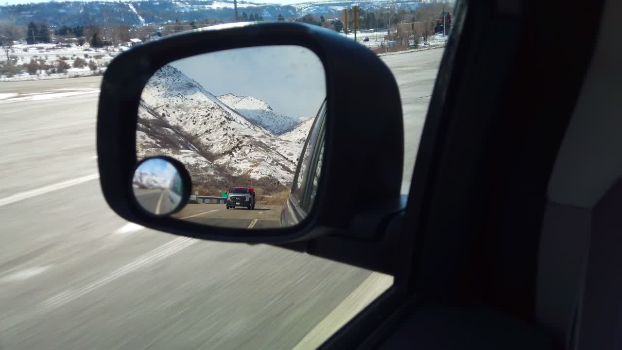 A rearview mirror on a car traveling in the winter time with Mountains in the background