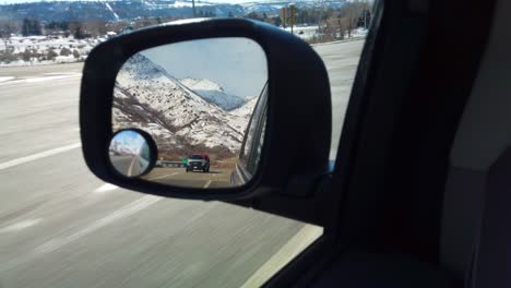 Ein-Rückspiegel-Eines-Autos,-Das-Im-Winter-Unterwegs-Ist,-Mit-Bergen-Im-Hintergrund