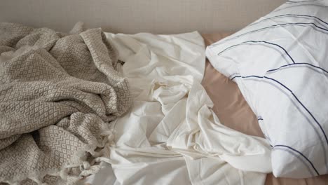 unmade bed with blanket and pillows