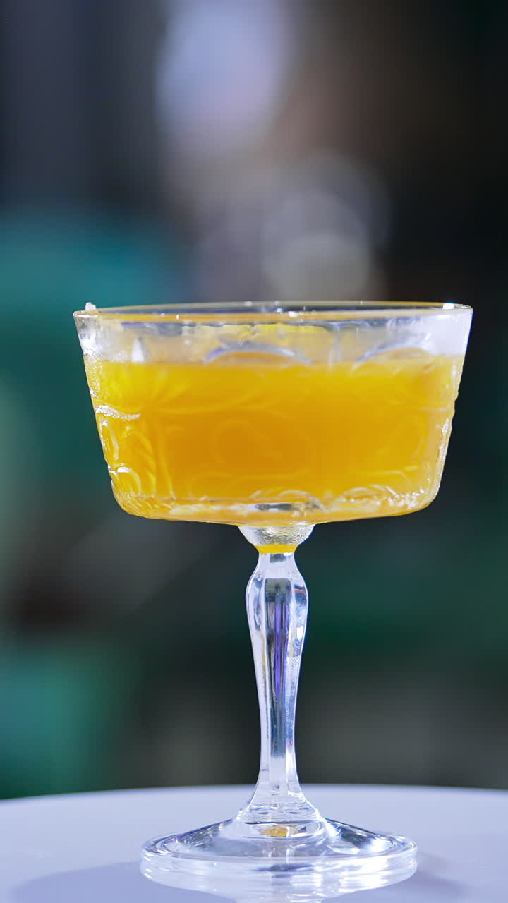 Glass goblet with savory drink. Orange alcohol cocktail on the rotating table. Close up. Blurred backdrop. Vertical video