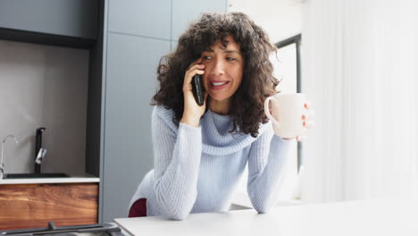 Happy-mature-caucasian-woman-drinking-coffee-and-talking-on-smartphone-at-home,-slow-motion