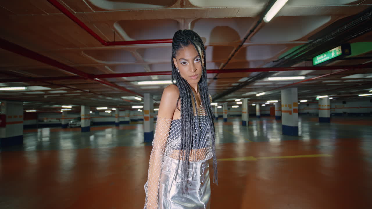 elegante modelo de dreadlocks pisando lugar de estacionamiento oscuro. morena posando