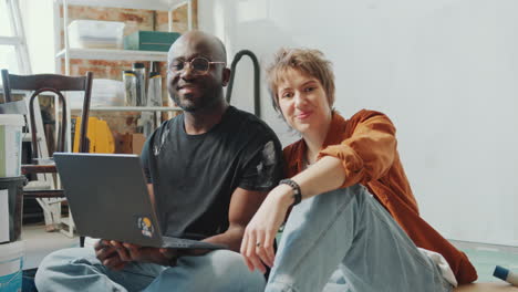 portrait of cheerful family couple with laptop in living room under renovation