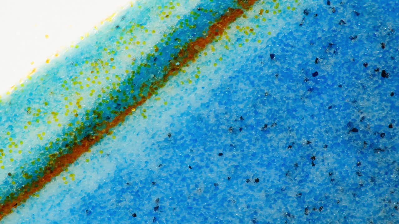 Abstract close-up view of a textured blue surface with green and yellow specks and an orange line