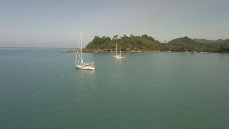 Aerial-view-of-sailing-Yachts-in-ocean-with-island-and-turquoise-ocean