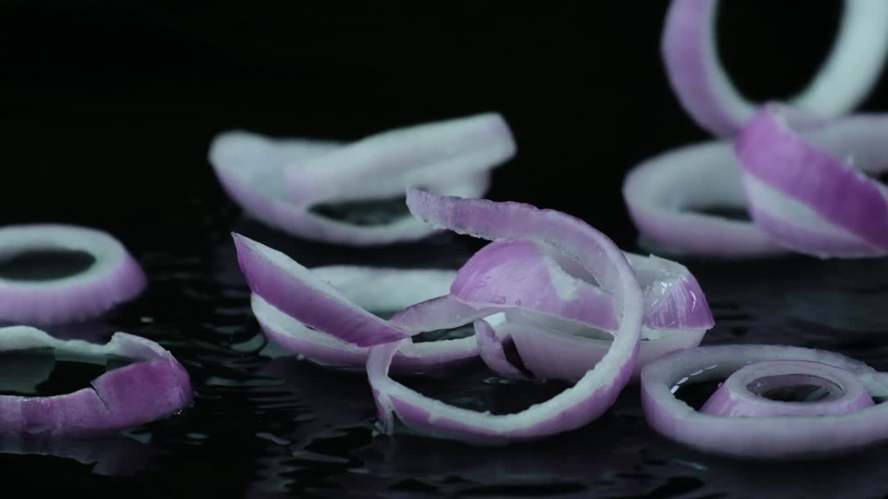 Slow motion raw sliced onion rings falling onto rippling water surface isolated on black background