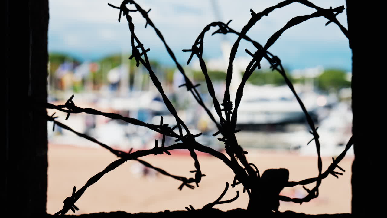 Close up of barbed wire loops with a blurred view of boats docked in a harbour in daylight