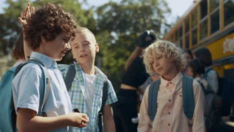 three school boys talking near school bus close up. happy pupils communicating