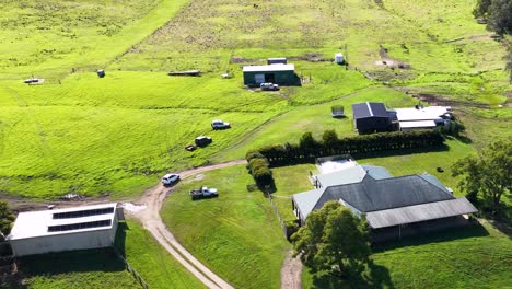 aerial footage of a rural property with buildings, vehicles, and lush green fields under bright sunlight