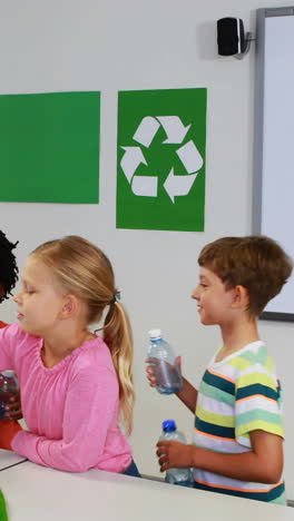 school kids putting bottle in recycle logo box in classroom