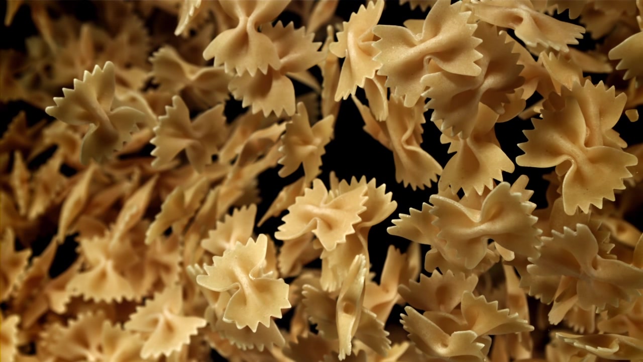 Pasta farfalle secca che cade al rallentatore su sfondo nero.