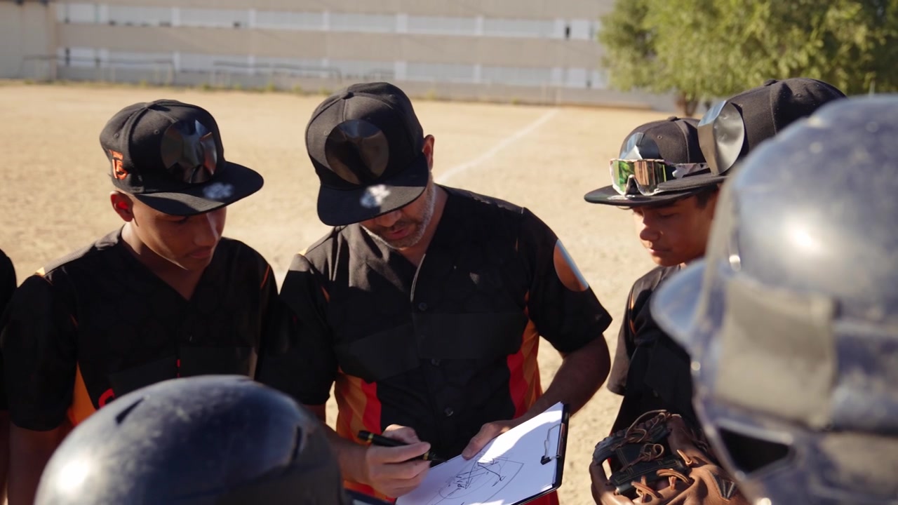 Entrenador de béisbol explicando estrategia a equipo juvenil en el campo.