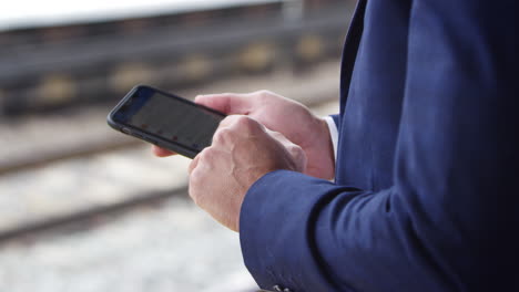 Cerca-Del-Empresario-En-El-Andén-Del-Ferrocarril-Enviando-Mensajes-De-Texto-Por-Teléfono-Móvil