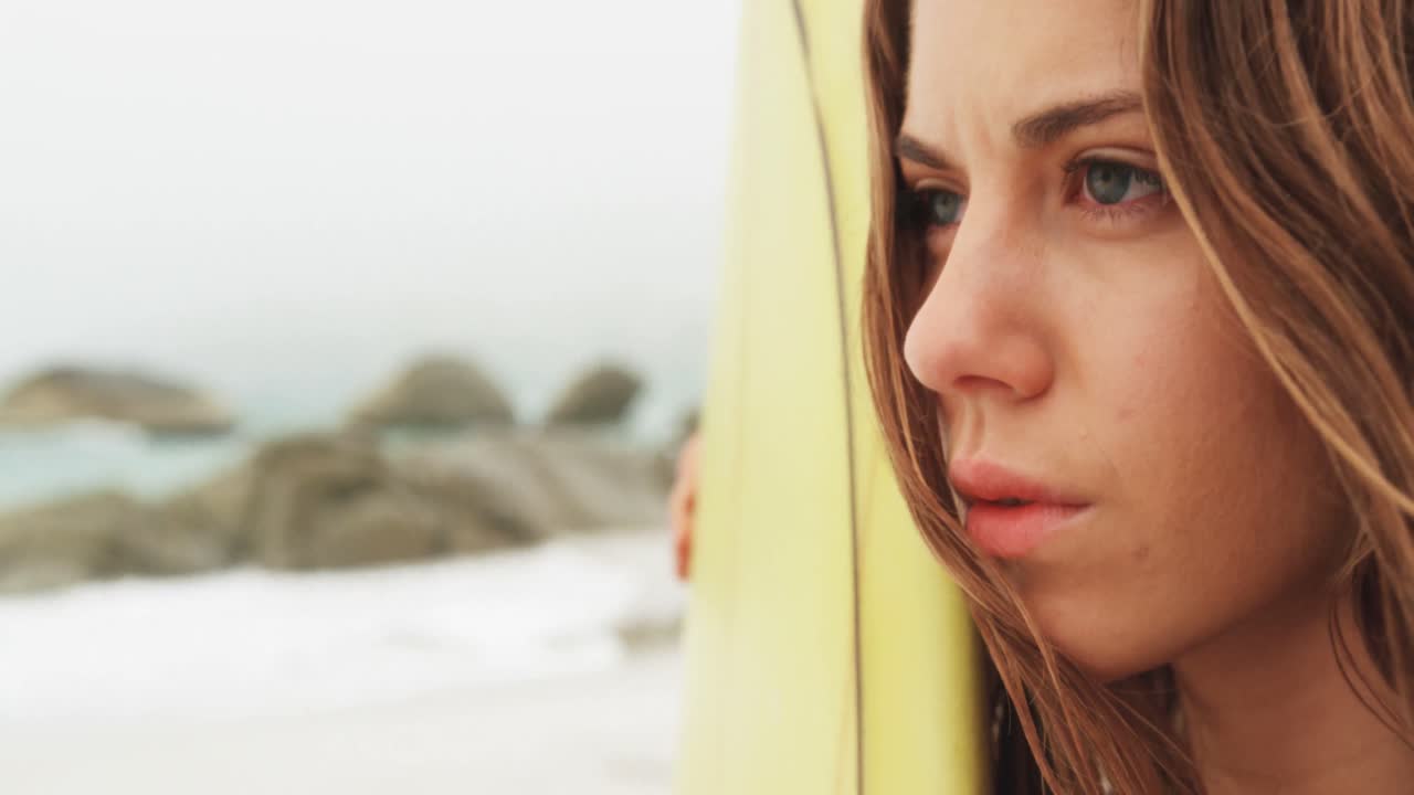 vista lateral de una surfista caucásica de pie con una tabla de surf en la playa 4k