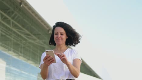 Sonriente-Empresaria-De-Mediana-Edad-Leyendo-Noticias-Desde-Un-Teléfono-Inteligente.