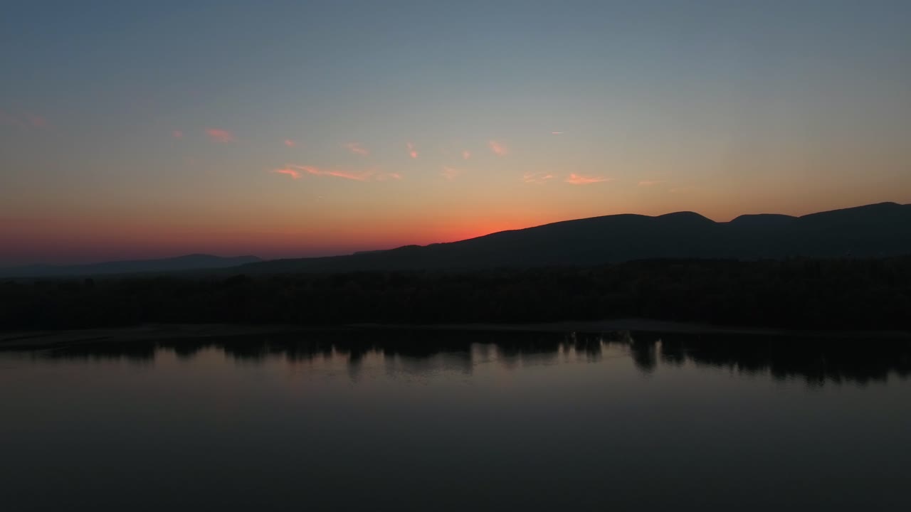 establishing shot of a sunset or sunrise over the mountains, with water and reflection