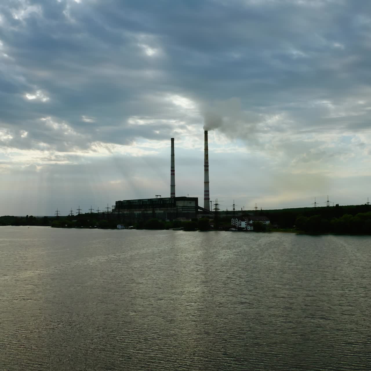 Environment pollution. Flight over the river water on industry background. Harmful factory at the bank of the river. Industrial chimneys with smoke in contrast with blue sky in the evening