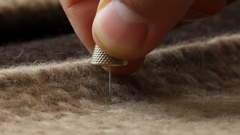 close-up of a hand using a thimble and needle on textured fabric