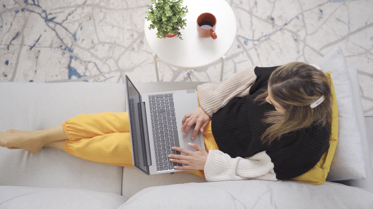 아름다운 여성이 소파에 앉아서 무 ⁇ 에 있는 노트북을 보고 문자 메시지를 보내고 영화를 보고 있습니다.