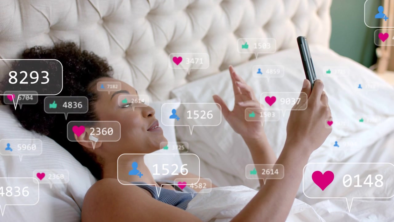 Social media creator lying on bed, speaking into phone, generating heart icons and follower counts