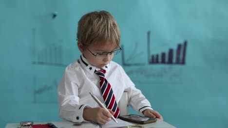 good looking, smart casual dressed child, blond boy with tie, working on tablet, taking notes and talking on the phone, business concept and idea
