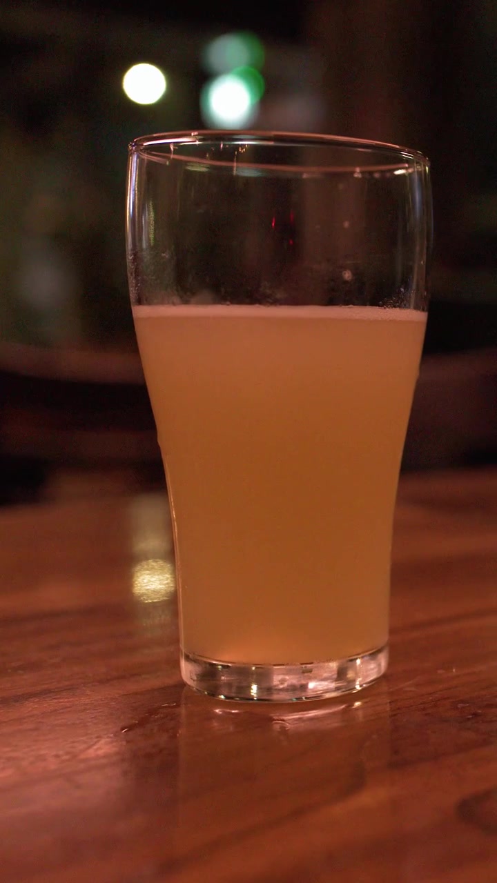 Static medium shot of a hazy pale ale in a glass on a wooden table