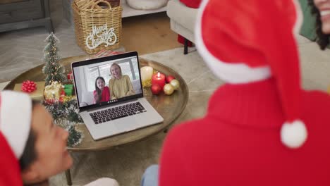 Diverse-family-with-santa-hats-using-laptop-for-christmas-video-call-with-happy-family-on-screen