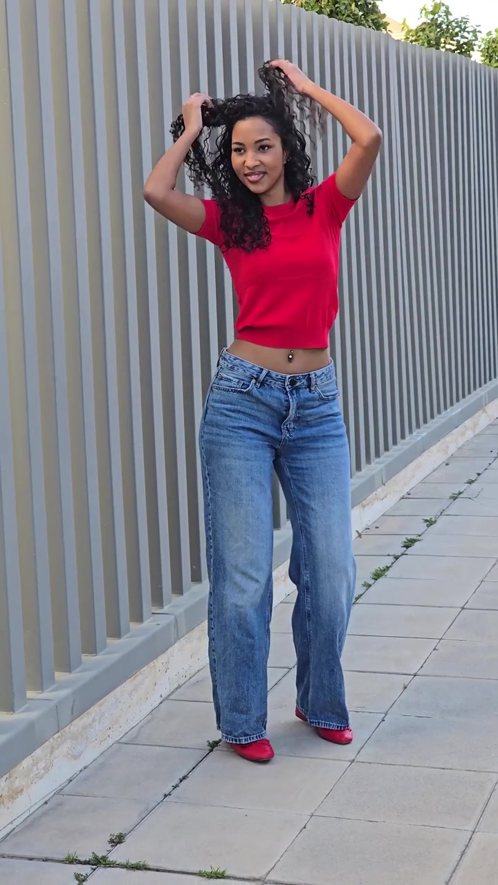 Una giovane donna con un top rosso brillante e jeans alla moda posa all'aperto in un ambiente vivace